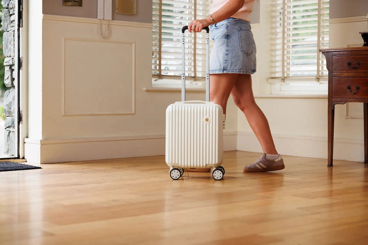 A low profile shot a woman walking to her front door, rolling her white Ryanair underseat hard case